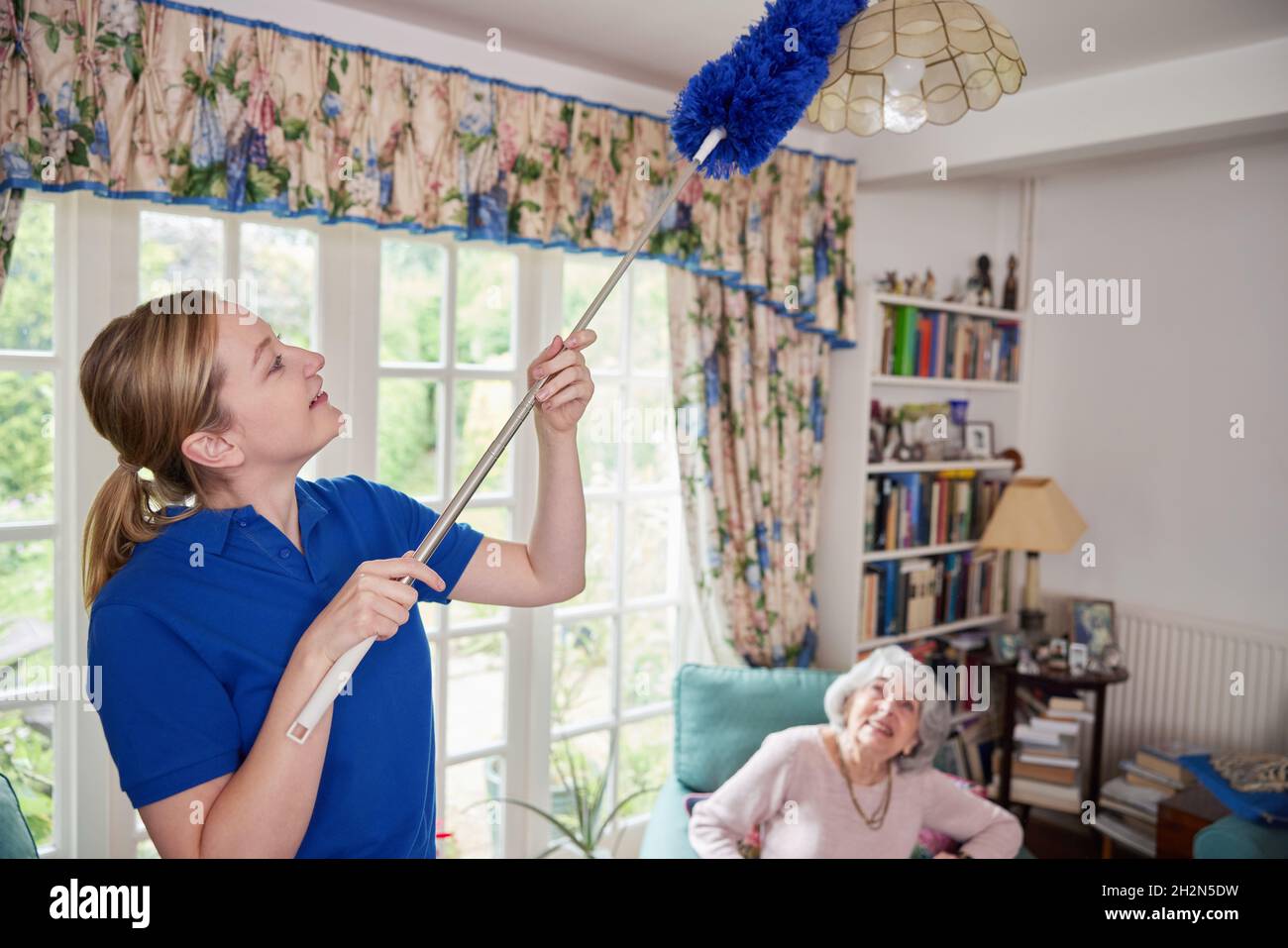 Weibliches Zuhause Hilfe Reinigung Haus, Wie Sie Stäubt Und Spricht Mit Älteren Frau Stockfoto
