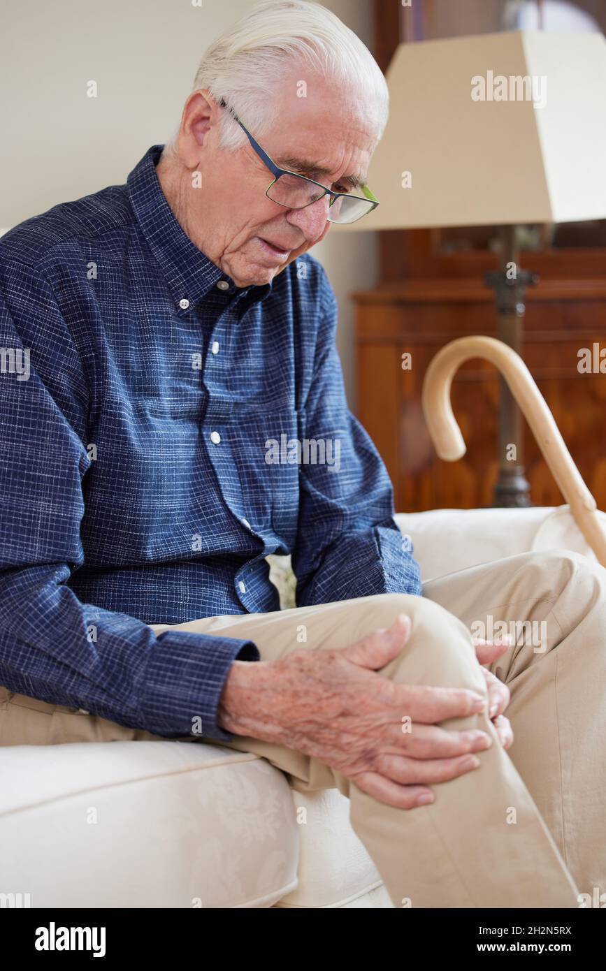 Älterer Mann, Der Zu Hause Auf Dem Sofa Sitzt Und An Knieschmerzen Durch Arthritis Leidet Stockfoto