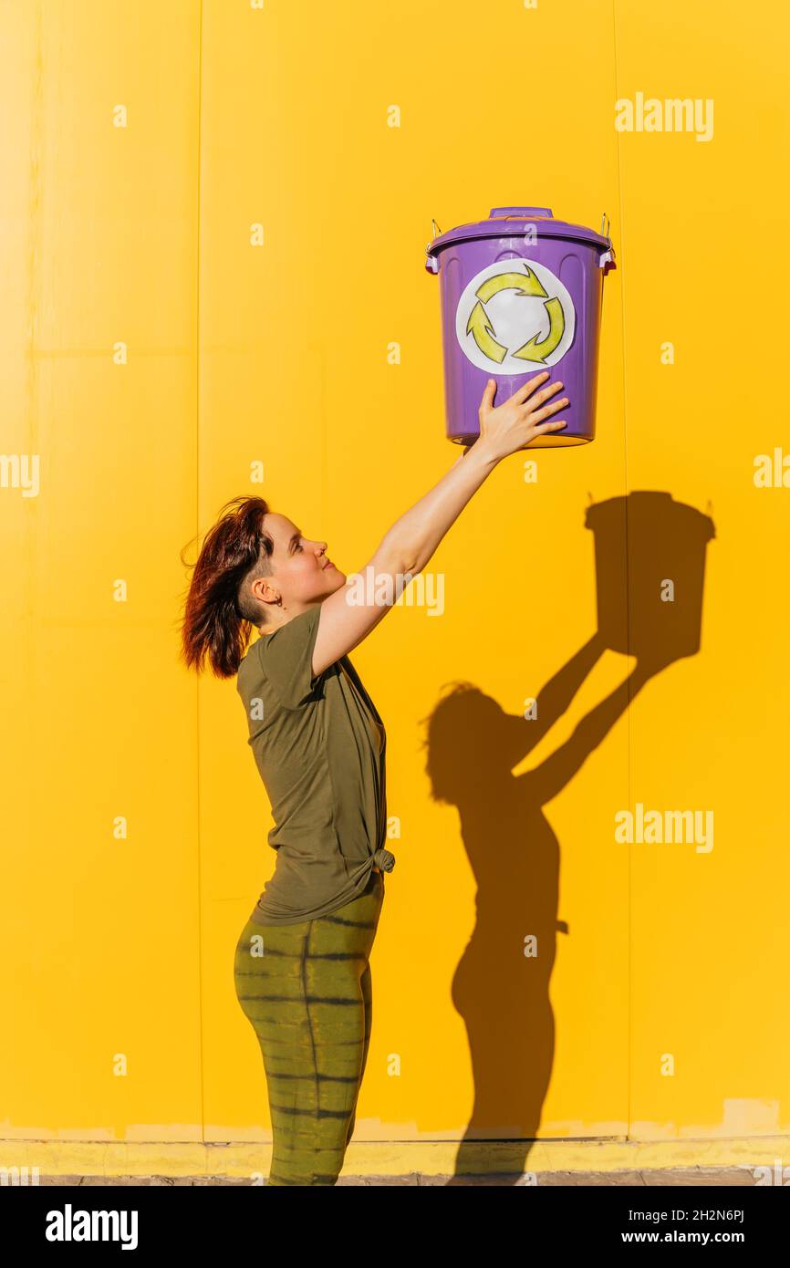Frau mit erhobener Hand hält Recyclingbehälter an sonnigen Tagen Stockfoto