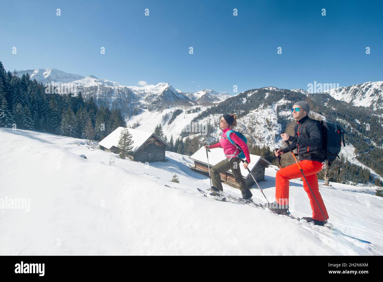 Das Paar genießt Kaffee, während es auf schneebedeckten Holzstämmen im Wald sitzt Stockfoto