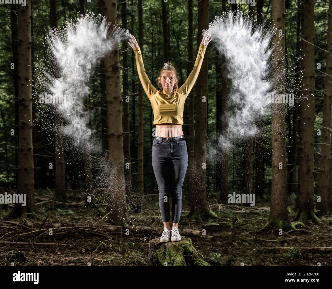 Sportlerin wirft weißes Mehl, während sie auf einem Baumstumpf im Wald steht Stockfoto