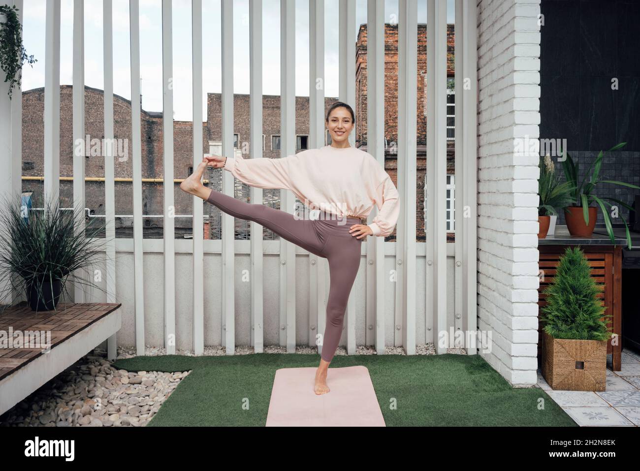 Lächelnde Frau, die auf der Terrasse Utthita Hasta Padangusthasana posiert Stockfoto