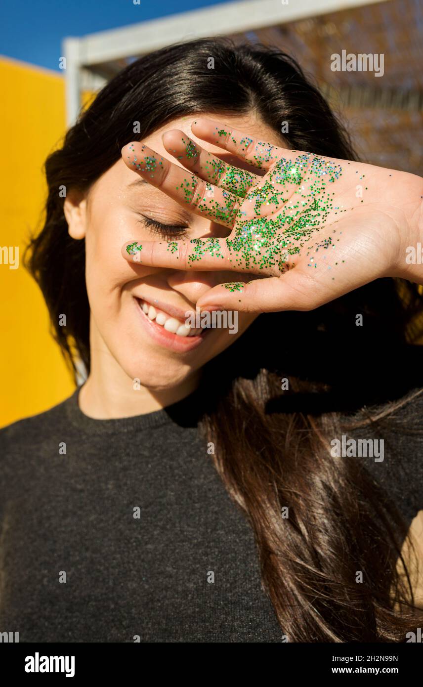 Lächelnde Frau bedeckt das Gesicht mit grünem Glitzer auf der Handfläche Stockfoto