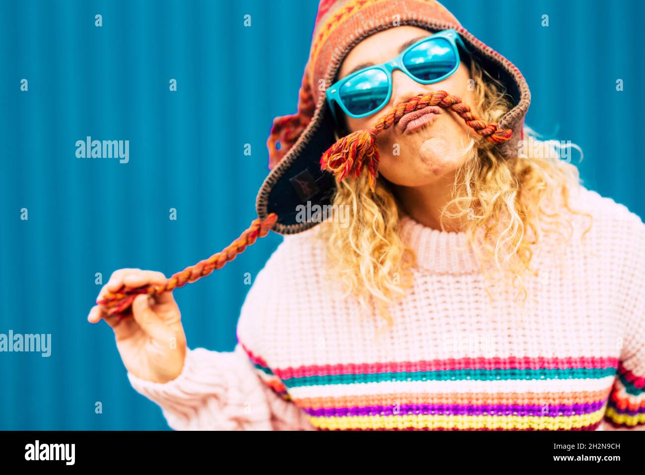 Verspielte Frau trägt Sonnenbrille und macht Schnurrbart aus Strickmütze Stockfoto