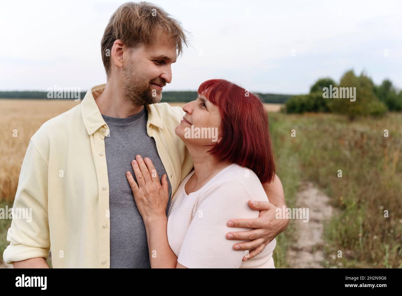 Paar mit Blume und Rechen küssen auf Weizenfeld Stockfoto