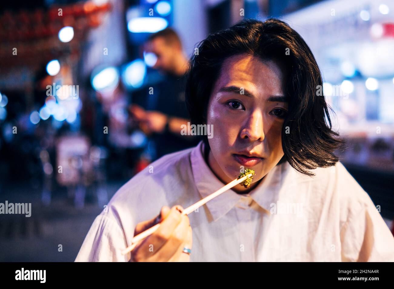 Junger Mann, der nachts mit Essstäbchen isst Stockfoto
