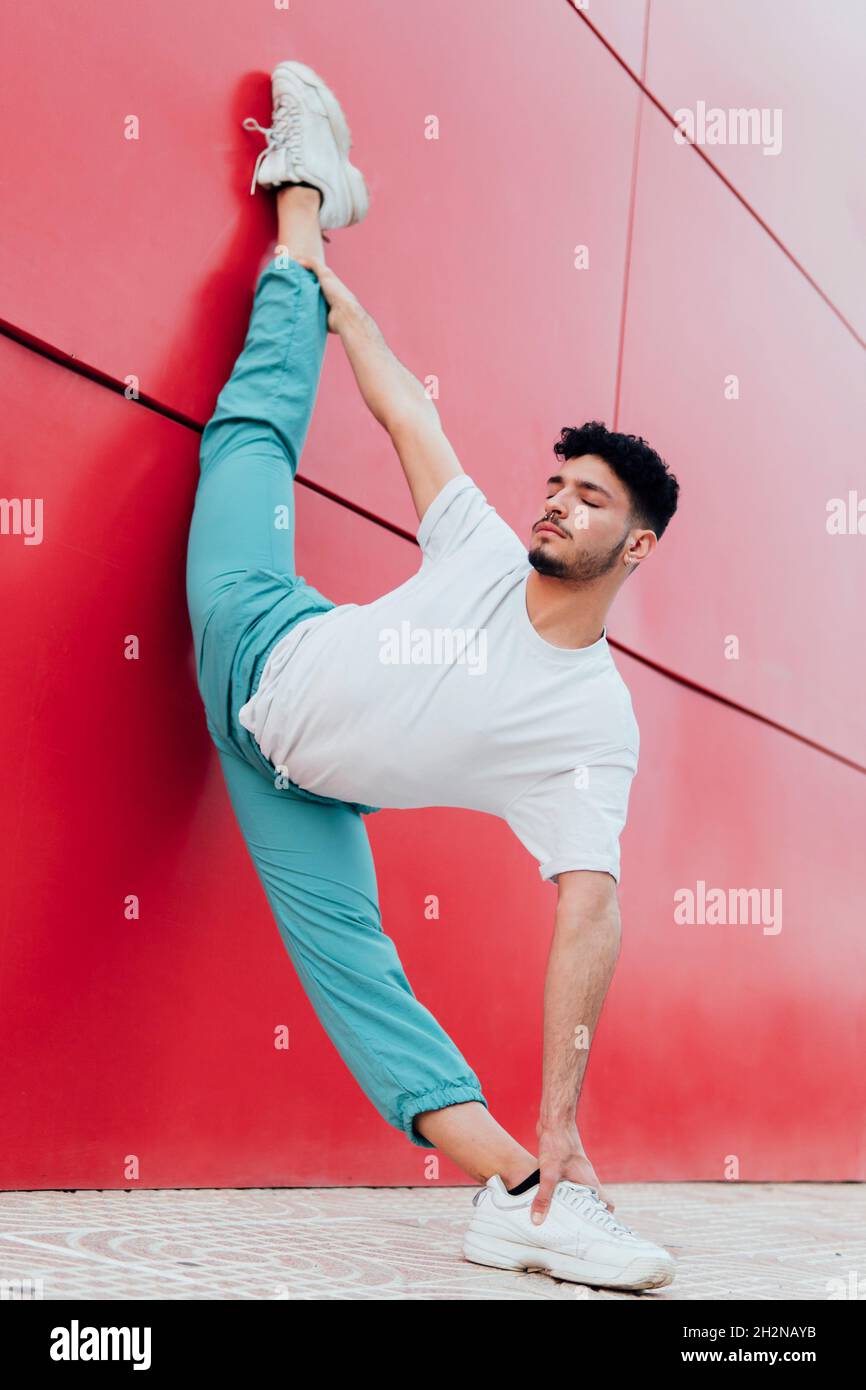 Männlicher Tänzer, der an der Wand lehnt und eine arabeske Position übt Stockfoto