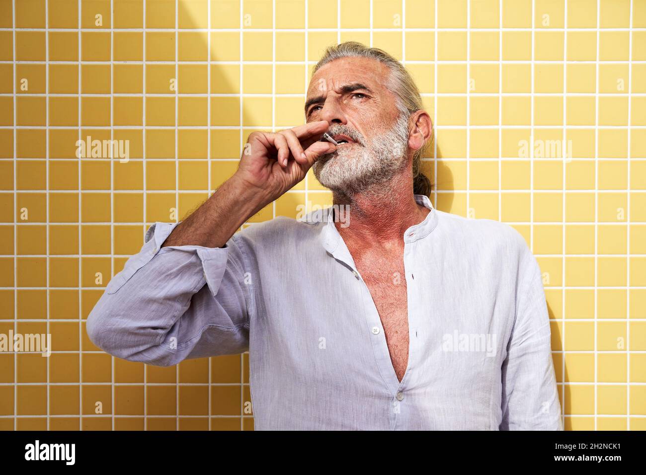 Reifer Mann, der vor der gelben Wand raucht Stockfoto