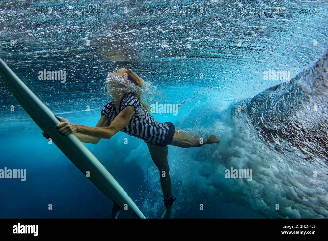 Junge Frau mit Surfbrett Schwimmen unter Meer Stockfoto
