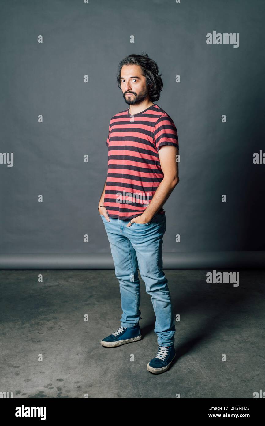 Mittelerwachsener Mann, der vor grauem Hintergrund mit Händen in Taschen steht Stockfoto