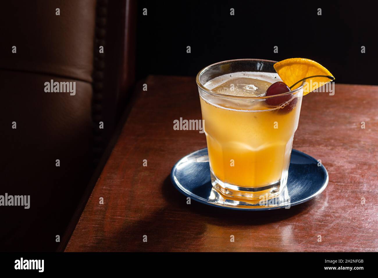 Amaretto Sour Cocktail Drink on the Rocks mit Orangen- und Kirschkrisen in der dunklen, luxuriösen Bar Stockfoto