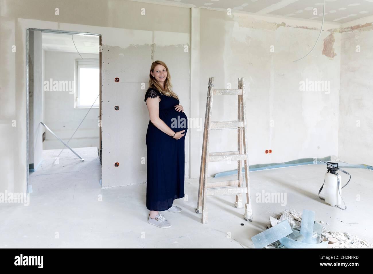 Schwangere berührt den Bauch, während sie am Fenster steht Stockfoto