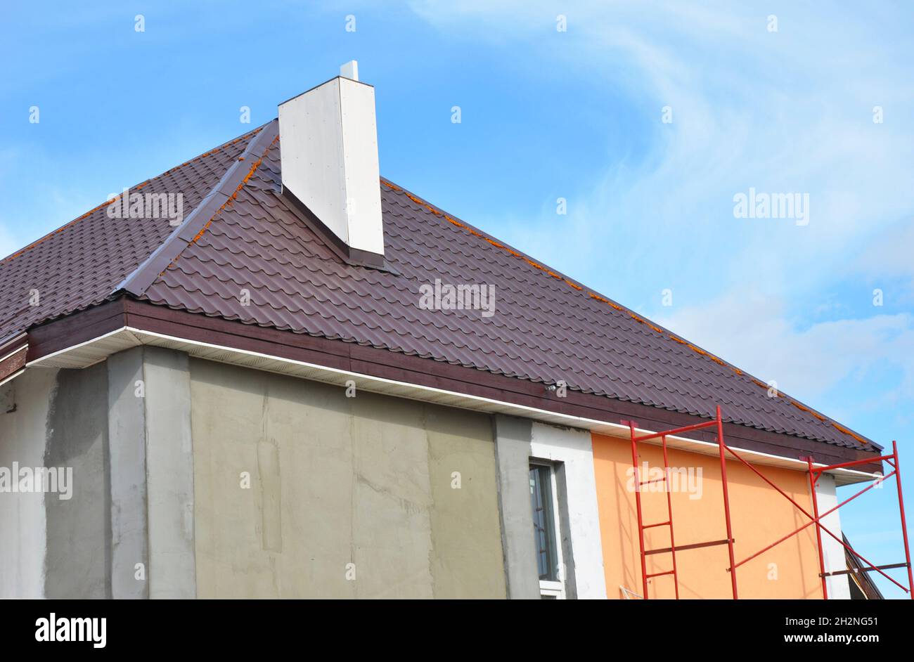 Dachkonstruktion aus Metall mit Kamininstallation, Stuck, Verputzen und Bemalung der Hauswand. Metalldächer Konstruktion mit Kunststoff-Soffits. Stockfoto