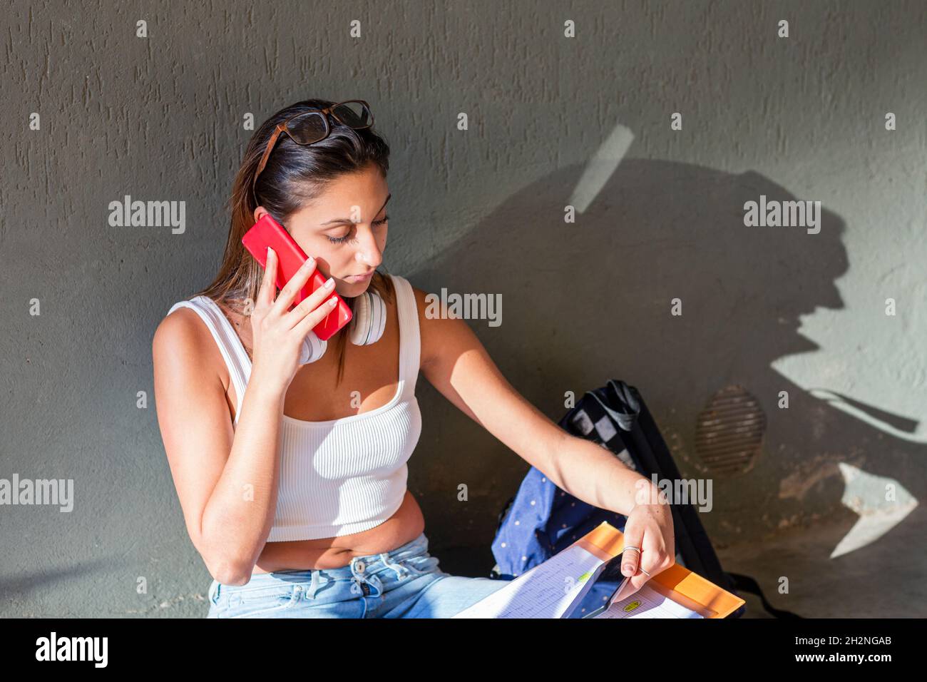Teenager mit Buch, das an der Wand auf dem Handy spricht Stockfoto