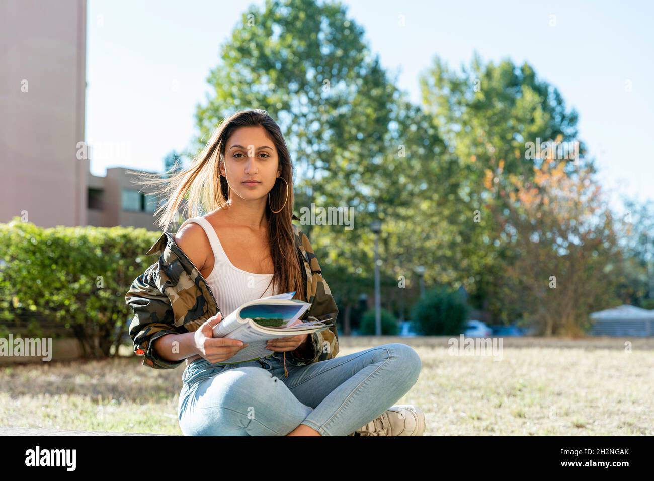 Weibliche Teenager hält Buch, während sie im Park mit gekreuzten Beinen sitzt Stockfoto