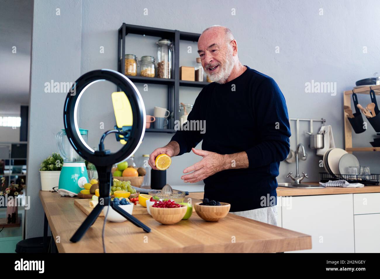 Älterer männlicher Vlogger mit Obstschale, der zu Hause über das Mobiltelefon filmte Stockfoto