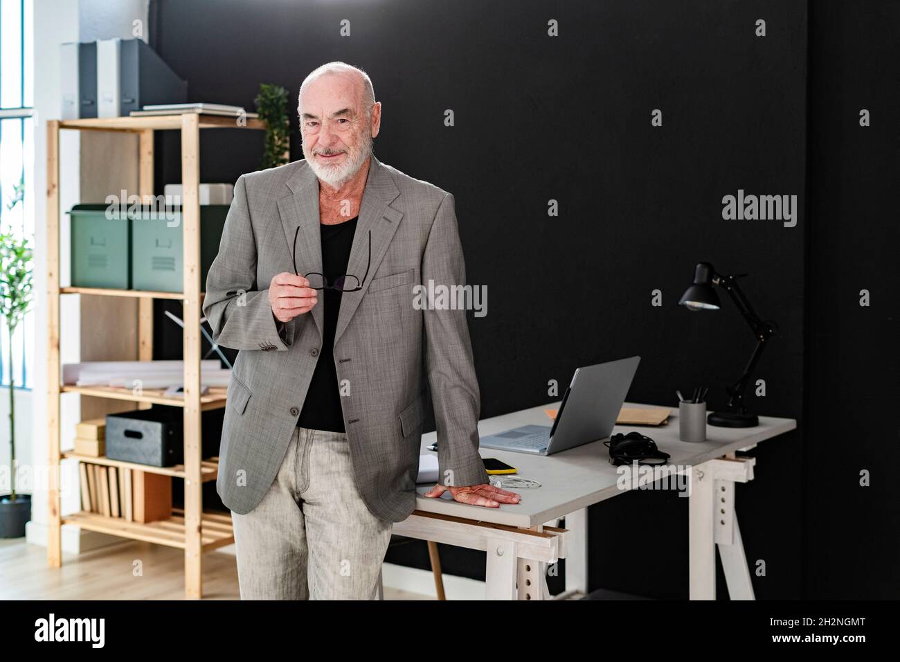 Lächelnder, älterer, männlicher Profi, der mit einem Laptop im Studio sitzt Stockfoto