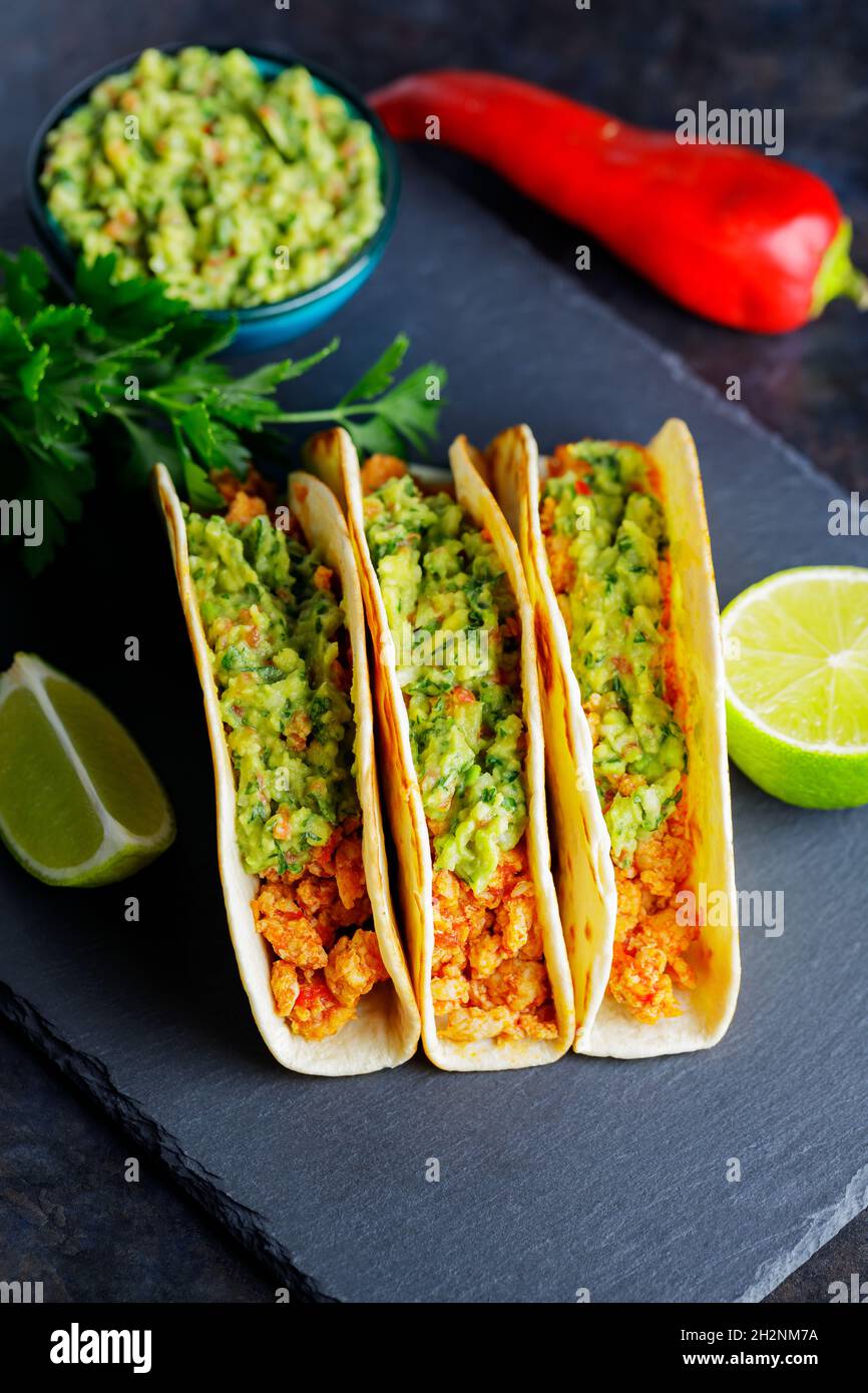 Tacos mit gebratenem Hackfleisch und Guacamole-Sauce auf dunklem Grund. Mexikanische Tacos und Zutaten auf einer Schiefertafel. Hispanische Küche Stockfoto