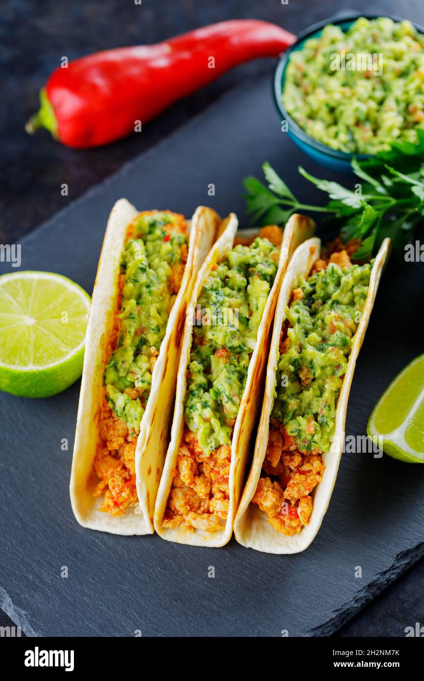 Tacos mit gebratenem Hackfleisch und Guacamole-Sauce auf dunklem Grund. Mexikanische Tacos und Zutaten auf einer Schiefertafel. Hispanische Küche Stockfoto