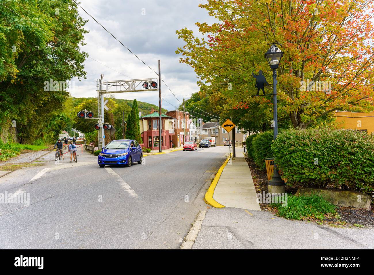 Glen Rock, PA, USA - 17. Oktober 2021: Fahrradfahrer, die das Parksystem des York County Heritage Rail Trail nutzen, warten auf den Verkehr, um eine Straße in der Innenstadt zu überqueren. Stockfoto