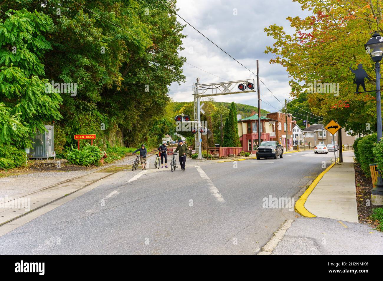 Glen Rock, PA, USA - 17. Oktober 2021: Fahrradfahrer, die das Parksystem des York County Heritage Rail Trail nutzen, warten auf den Verkehr, um eine Straße in der Innenstadt zu überqueren. Stockfoto