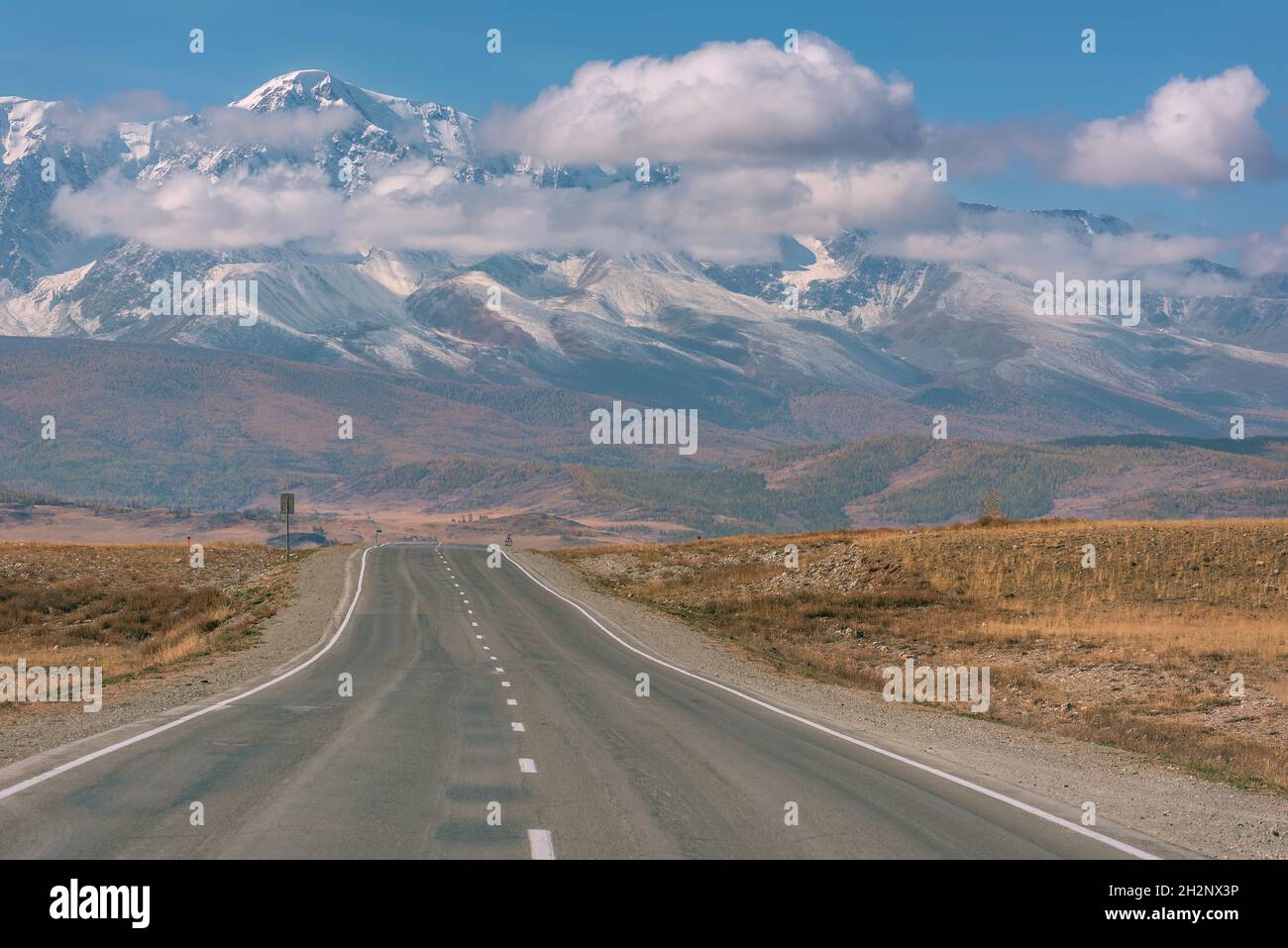Schöner Herbstblick von einer asphaltierten Straße auf die mit Schnee und Wald bedeckten Berge vor dem Hintergrund des blauen Himmels und der Wolken. Altai, Russland Stockfoto