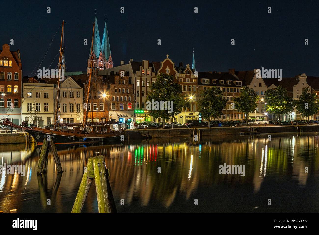 Spiegelungen der Nachtlichter der Stadt Lübeck an der Trave mit einem festfahrenden Segelschiff. Lübeck, Land Schleswig-Holstein, Deutschland Stockfoto