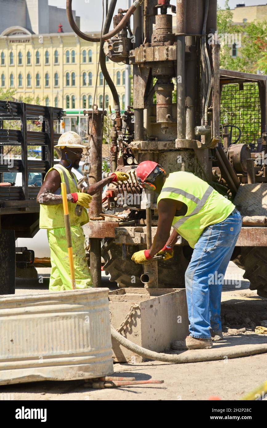 Zwei afroamerikanische Bauarbeiter bohren sicher ein Loch im Stadtzentrum, das an den Wisconsin River, Urban Renewal, Milwaukee, Wisconsin, USA, angrenzt. Stockfoto