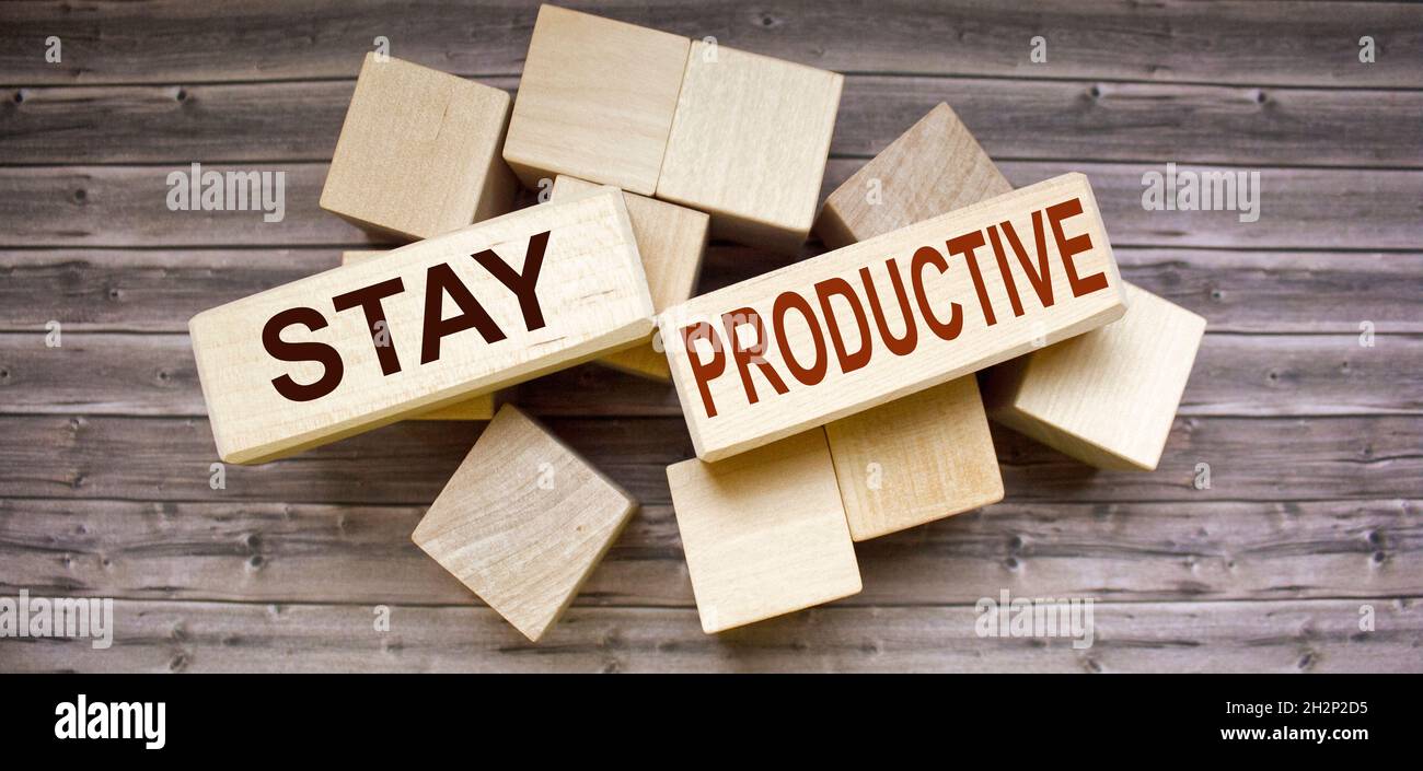 Konzeptuelles Image. Text PRODUKTIV BLEIBEN Erfolgskonzept auf Holzblöcken und braunem Tisch. Stockfoto