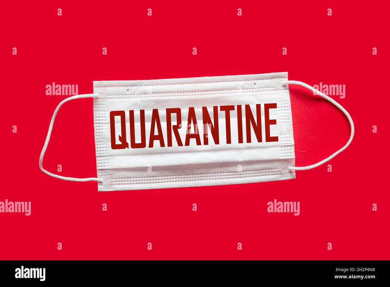 Chirurgische Maske Schutzmaske mit der Aufschrift QUARANTÄNE, auf rotem Hintergrund. Ein Ausbruch des chinesischen Coronavirus COVID-19. Stockfoto