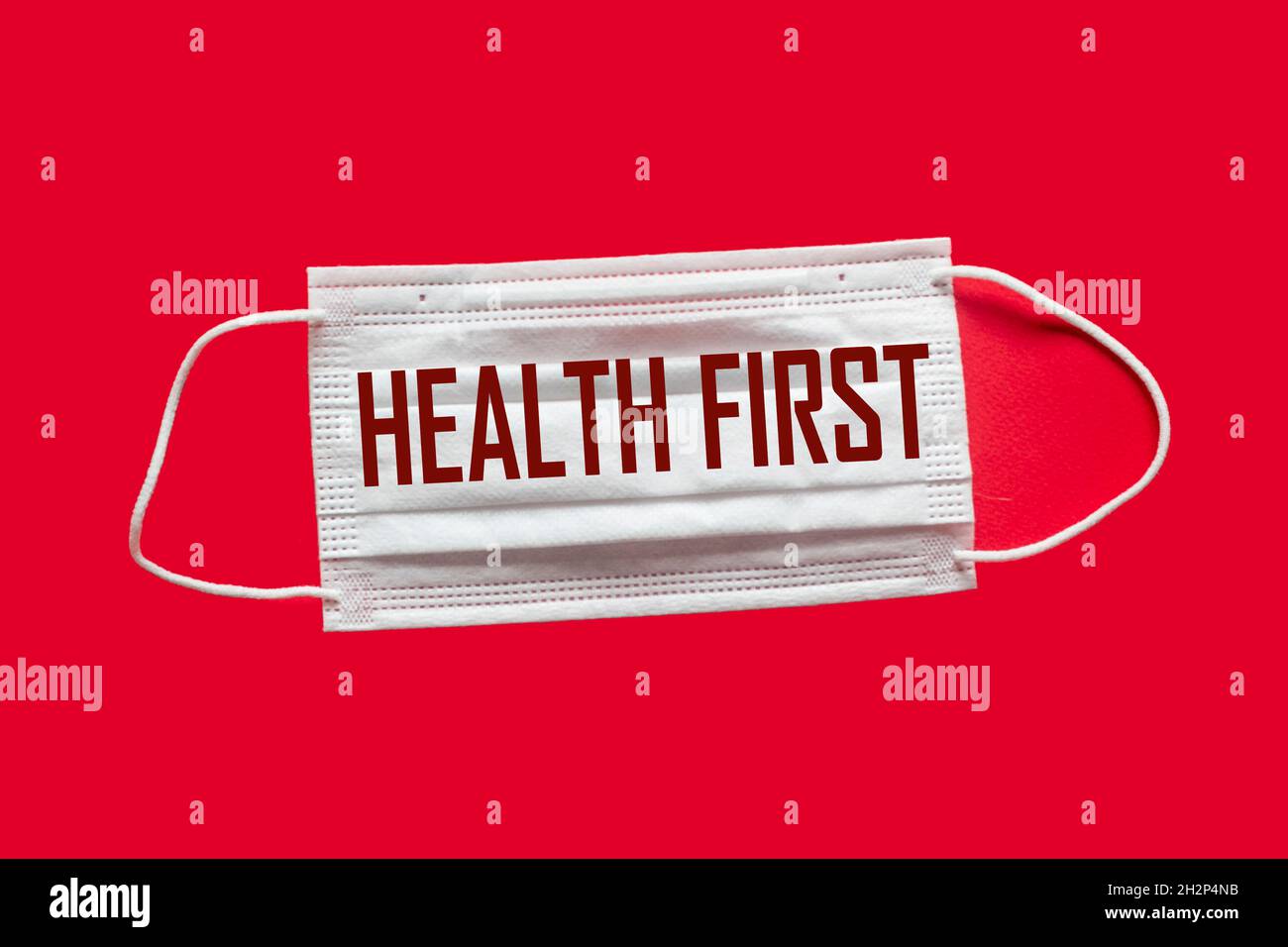 Medizinische Maske mit dem Text Gesundheit zuerst, auf rotem Hintergrund. Weltgesundheitstag. Gesundheitskonzept. Für Text platzieren. Weichfokus. Blick von oben. Stockfoto