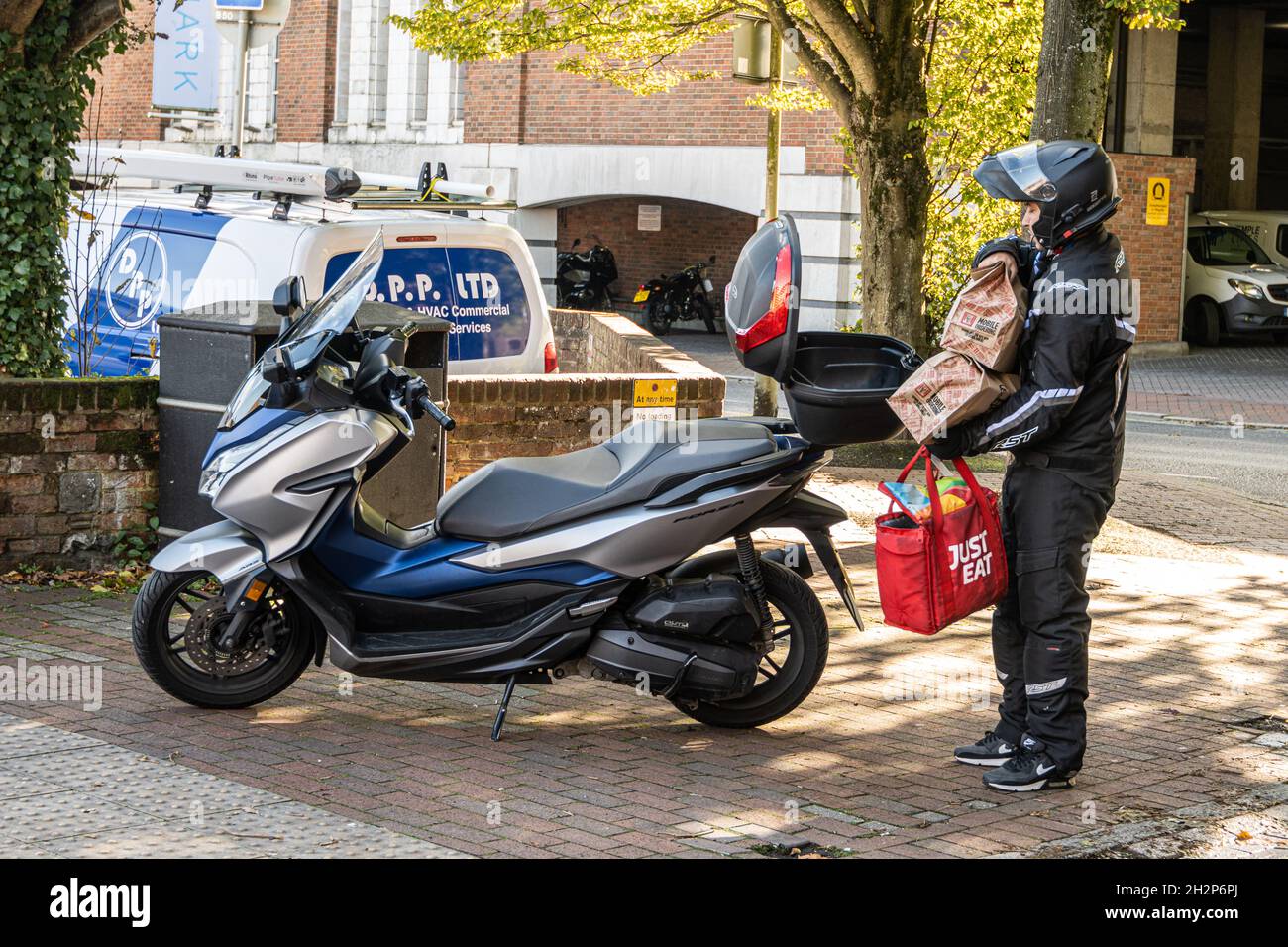Ein Fahrer, der Essen zum Mitnehmen liefert, trägt Befehle zu seinem Motorrad. Winchester, Hampshire, Großbritannien Stockfoto
