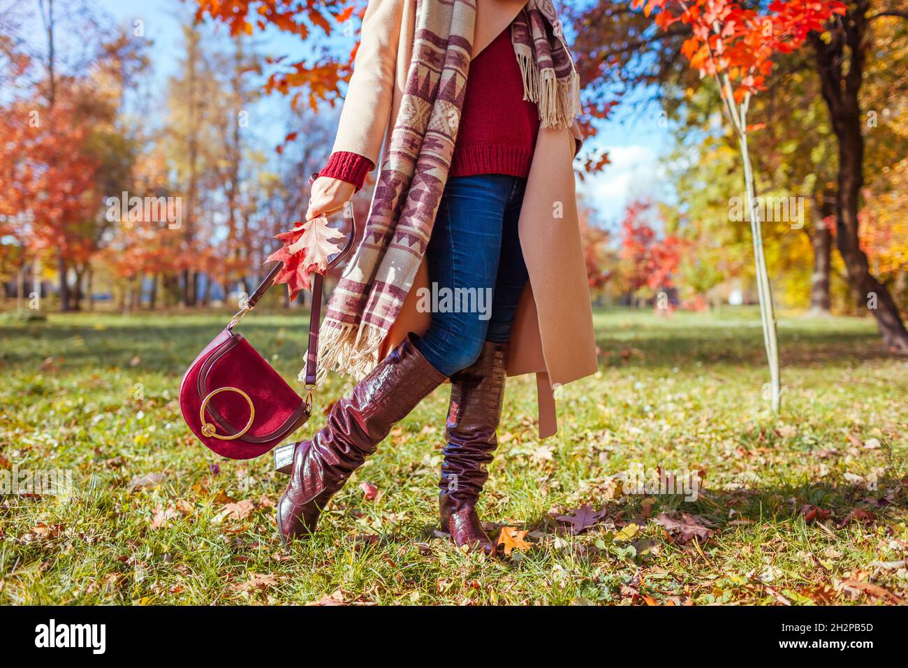 Modische Frau trägt stilvolle Kleidung Schuhe und Accessoires zu Fuß im  Herbst Park. Herbst-Outfit für Damen. Trendige kniehohe Stiefel, Mantel und  Burgunder Stockfotografie - Alamy