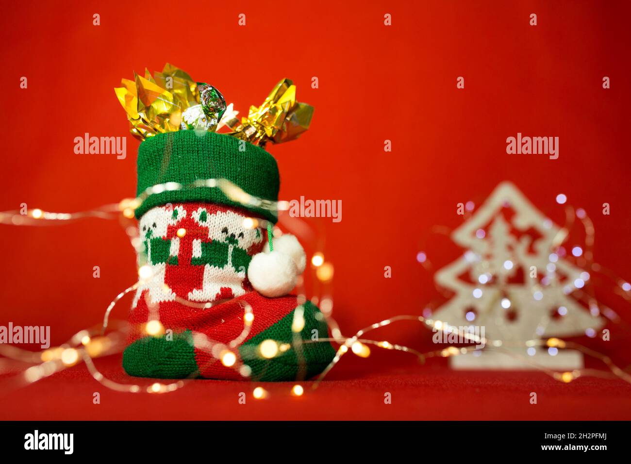 Neujahrs- und Weihnachtskarte auf rotem Hintergrund. Stiefel mit Süßigkeiten und Weihnachtsbeleuchtung. Inhalt zum Nikolaustag. Stockfoto