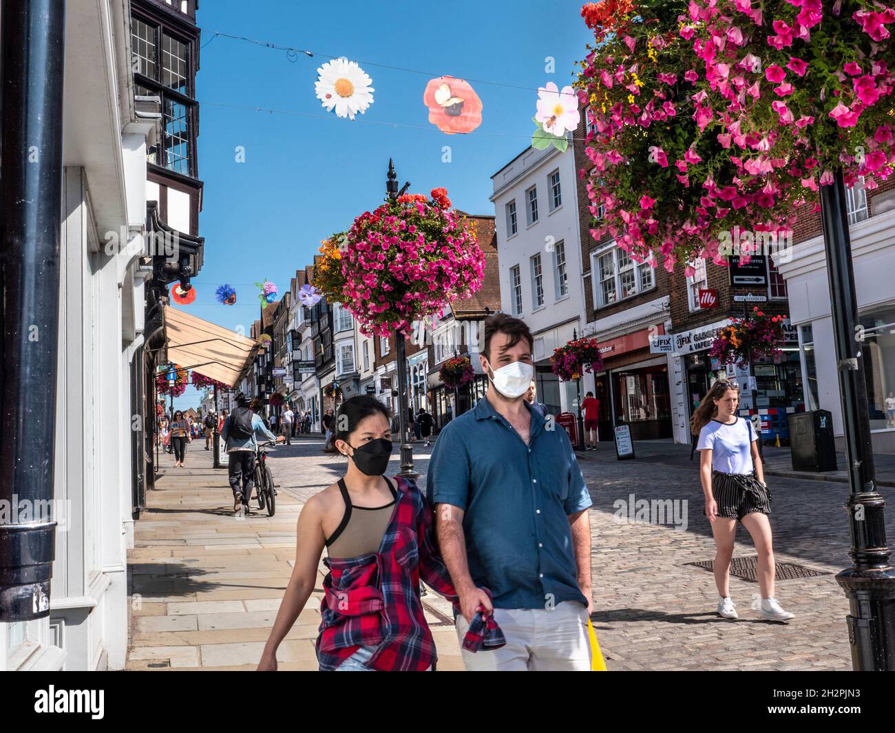 Guildford High Street mit einigen Einkäufern, die Covid-Gesichtsmasken tragen. Blumenkörbe im Herbst und farbenfrohe Banner der Saison in klarem, blauem, warmem Sonnenschein Stockfoto