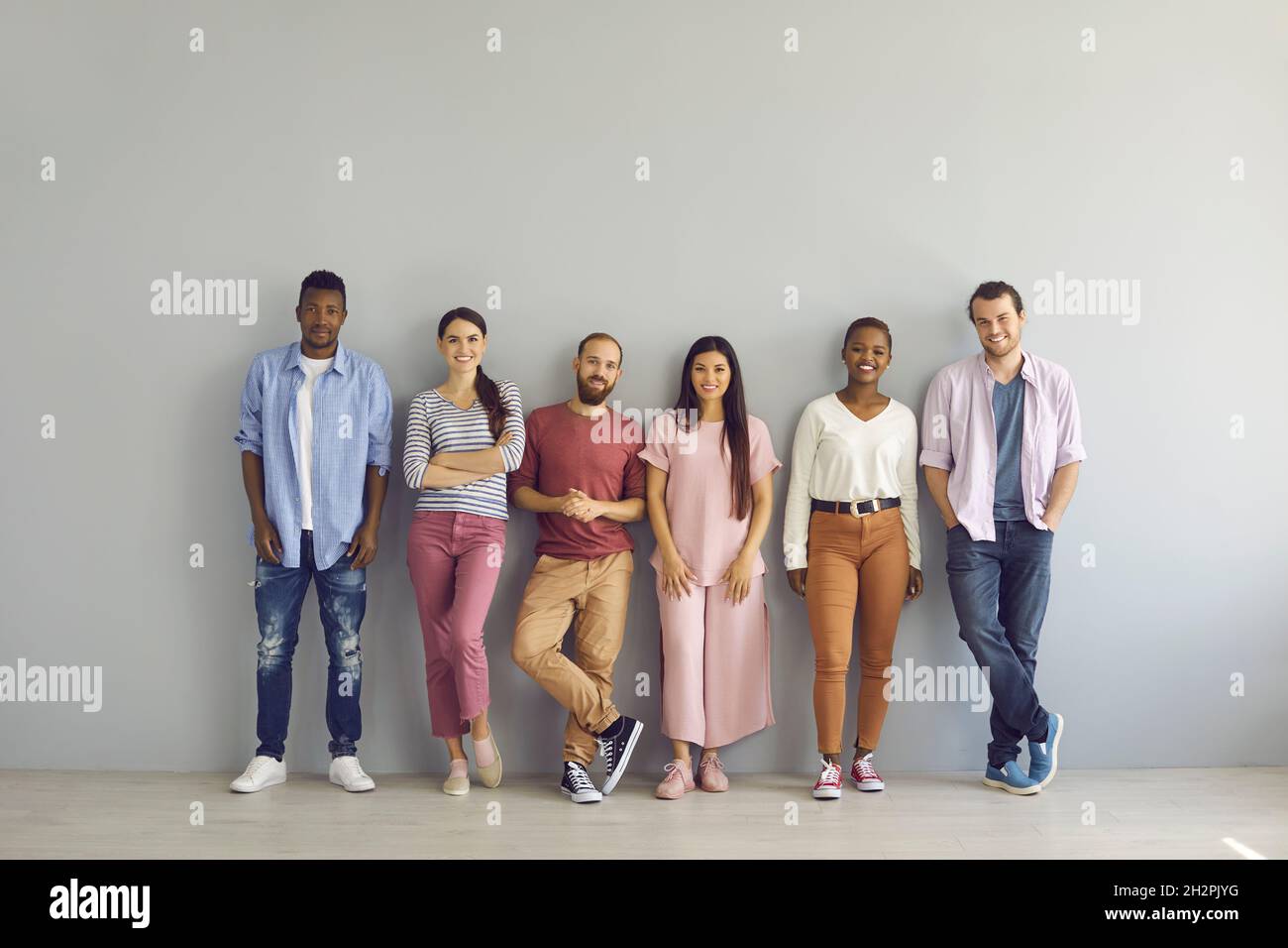 Porträt einer Gruppe lächelnder multirassischer Menschen, die in einer Reihe auf einem hellen Wandhintergrund stehen. Stockfoto