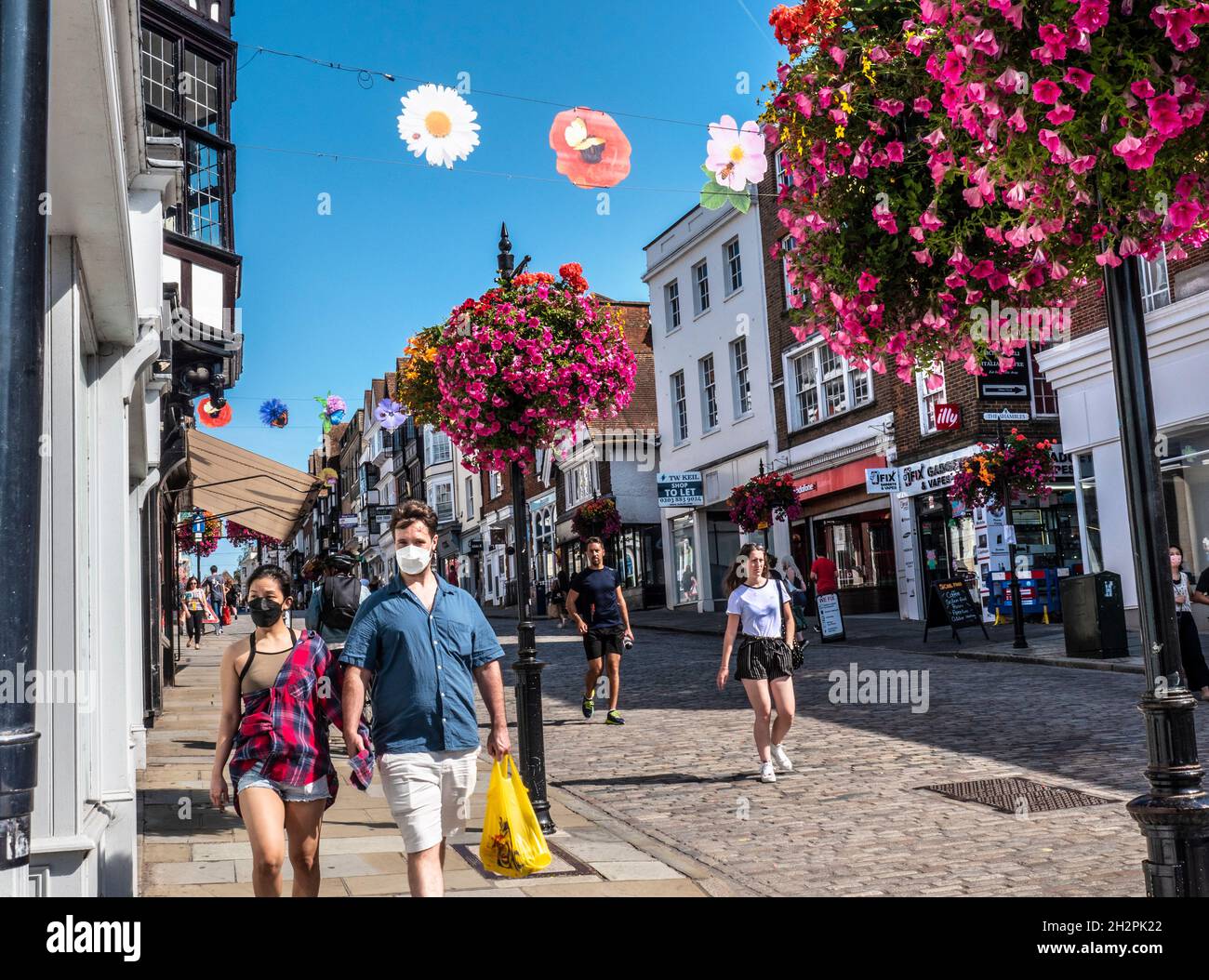 Guildford High Street mit einigen Einkäufern, die Covid-Gesichtsmasken tragen. Blumenkörbe im Herbst und farbenfrohe Banner der Saison in klarem, blauem, warmem Sonnenschein Stockfoto
