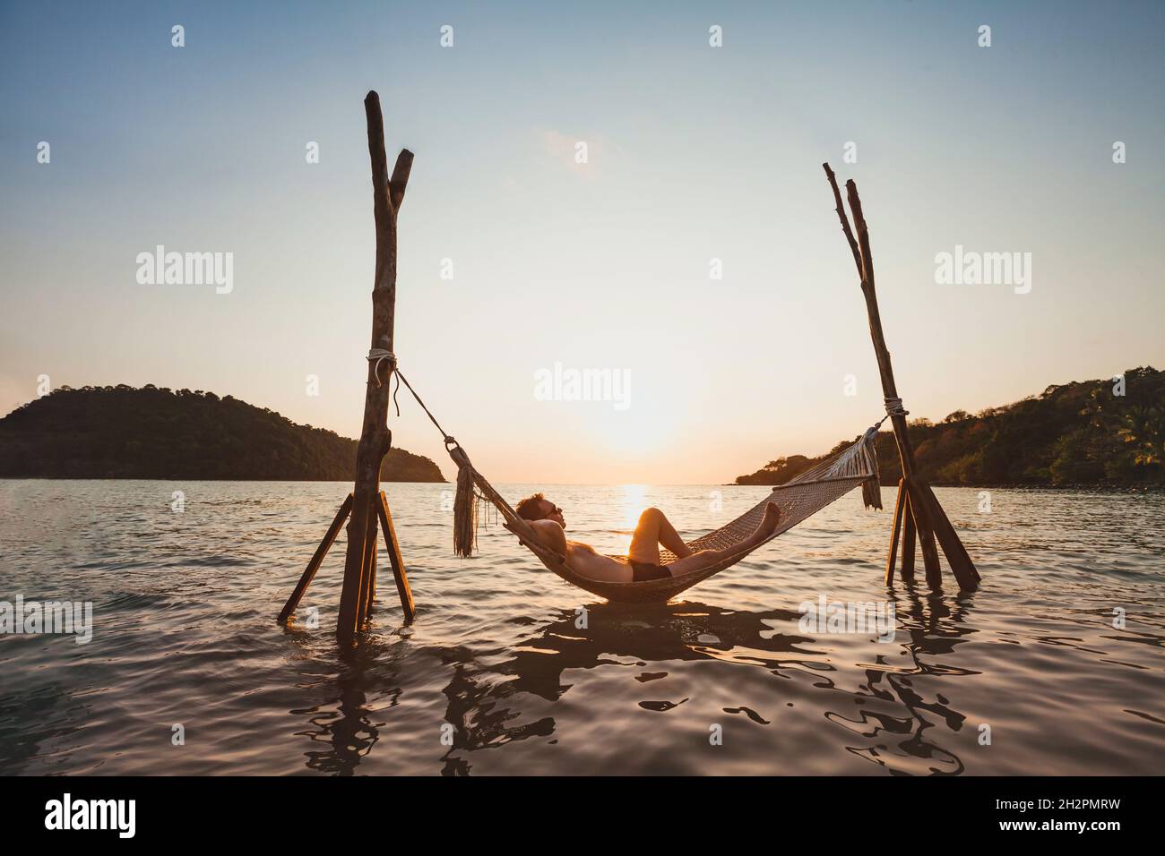 Strandurlaub, Entspannung in der Hängematte bei Sonnenuntergang, paradiesische Inselferien, glücklicher Mann Tourist, der sich ausruhen und das Leben genießen kann Stockfoto Strandurlaub, Entspannung in der Hängematte bei Sonnenuntergang, paradiesische Inselferien, glücklicher Mann Tourist, der sich ausruhen und das Leben genießen kann Stockfoto