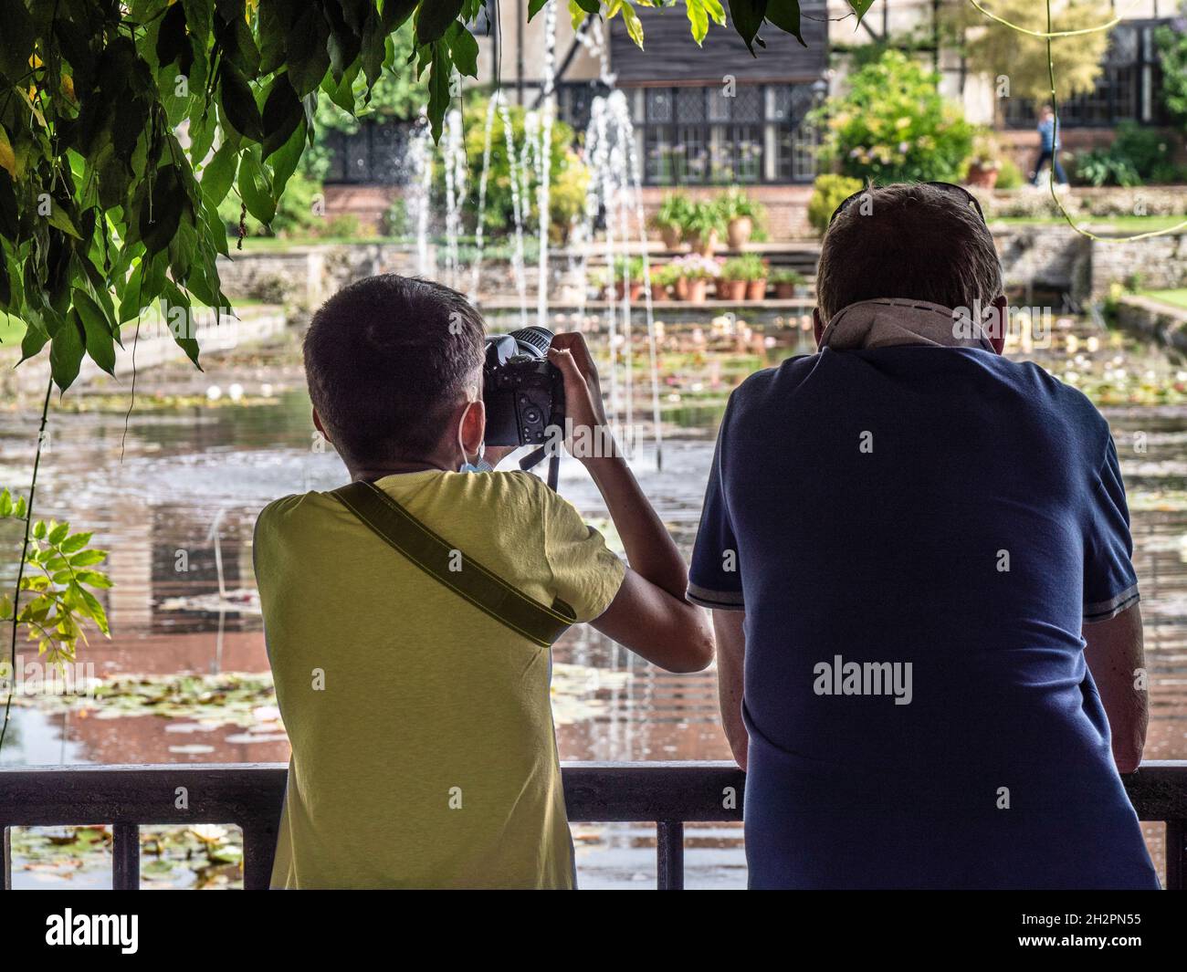 Kleiner Junge, 10-13 Jahre mit seinem Vater, der digitale Bilder des lilly-Teichs und der Springbrunnen mit seiner Spiegelreflexkamera in Wisley Gardens Surrey UK machte Stockfoto