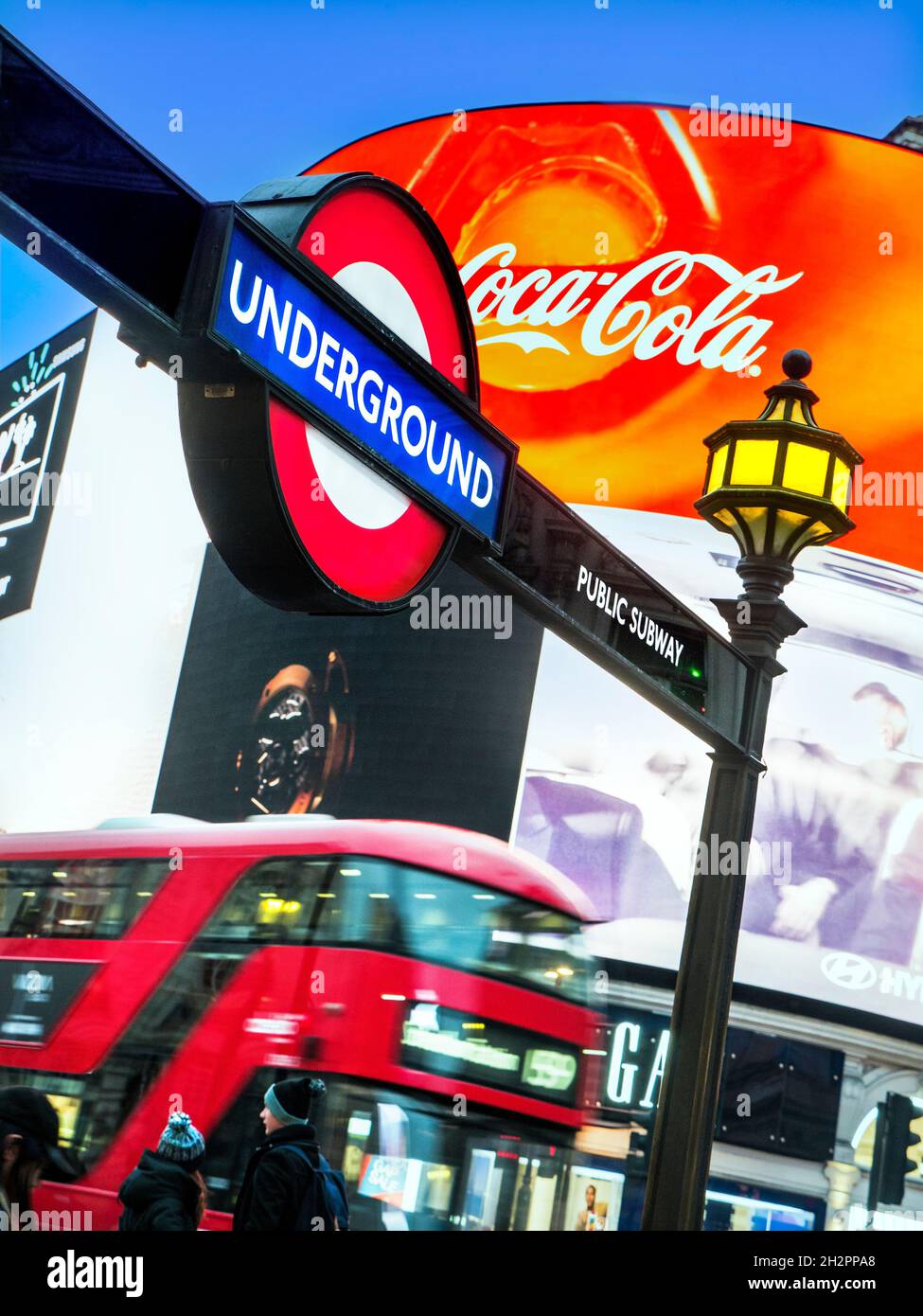 London Piccadilly Circus mit U-Bahn traditionelle U-Bahn-U-Bahn-Schild & beleuchteten Coca Cola Neon digitale Plakatwand Banner hinter und verschwommen roten Low Emission Hybrid London Bus in der Dämmerung Piccadilly London UK Stockfoto