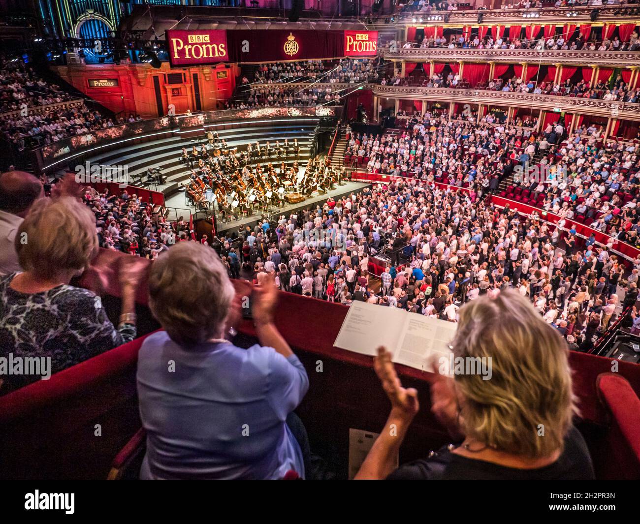 HINTER London UK verbirgt SICH DER AUFTRITT der BBC PROMS mit dem klatschenden Publikum, das von einer luxuriösen roten Velours-Privatbox auf die Zuschauer- und Orchesterbühne klatscht Stockfoto
