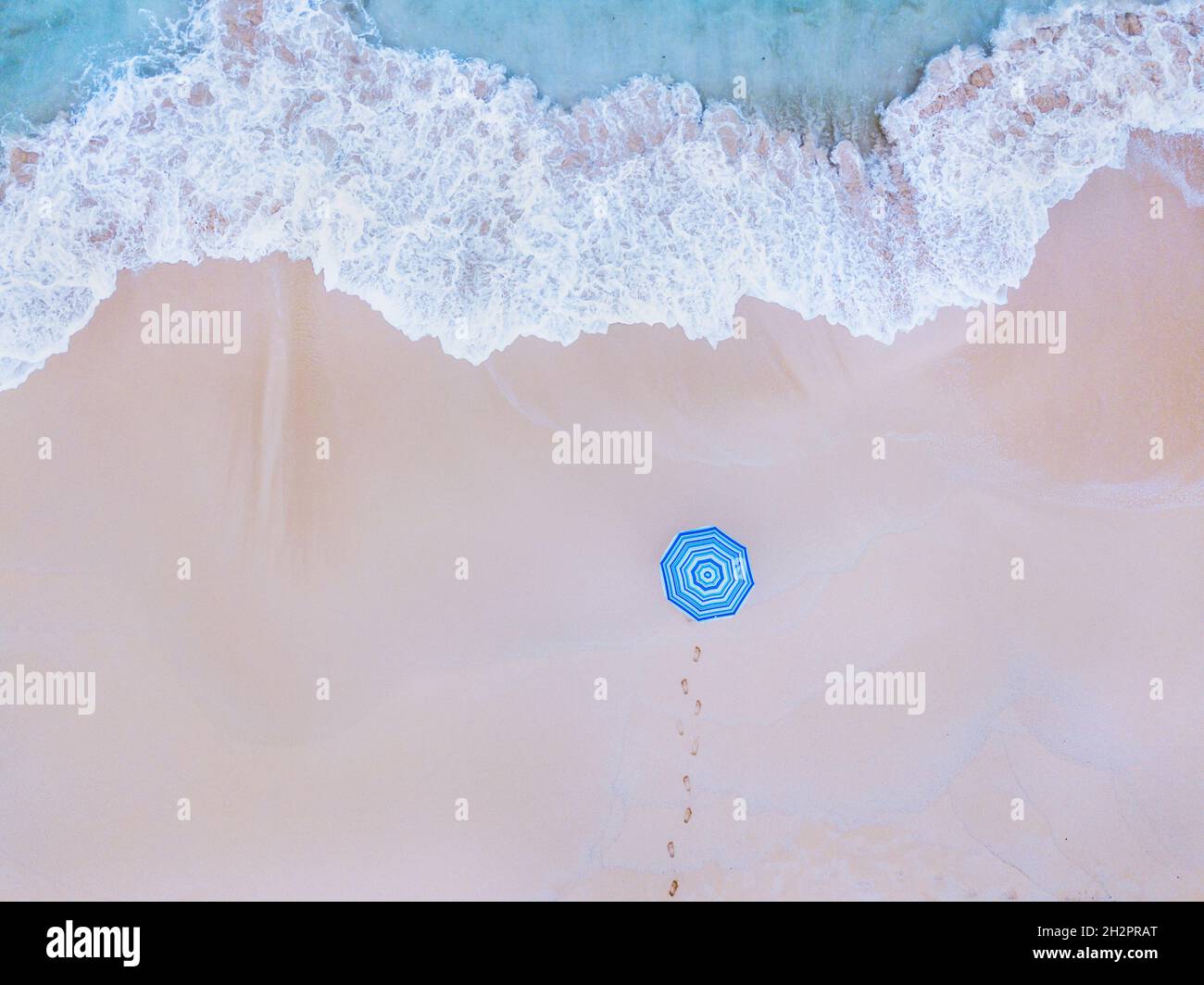 Reisen Sie zum wunderschönen Strand, Urlaub, Urlaub auf Paradise Island, Luftaufnahme von oben auf die Meereswelle und Person mit blauem Sonnenschirm. Stockfoto Reisen Sie zum wunderschönen Strand, Urlaub, Urlaub auf Paradise Island, Luftaufnahme von oben auf die Meereswelle und Person mit blauem Sonnenschirm. Stockfoto