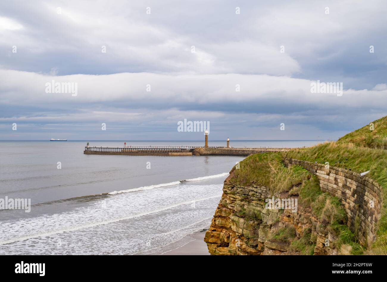 Ein entfernter Whitby West Pier oder Steg, der an einem trüben und bewölkten Herbsttag von den Klippen gefangen wurde Stockfoto