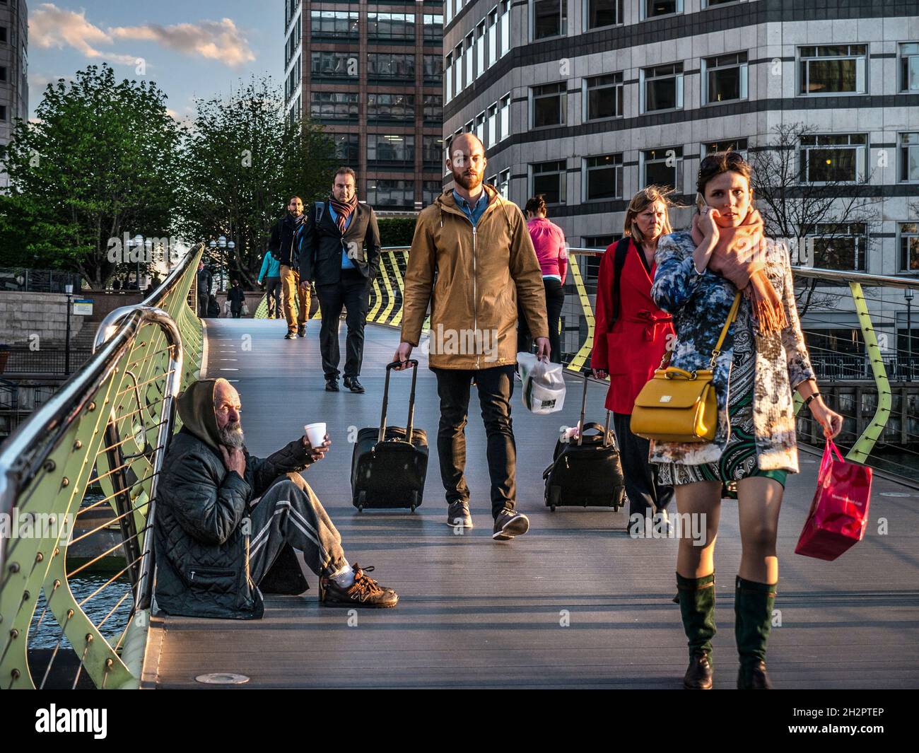 CITY WORKERS BETTELN CUP BETTLER CITY Canary Wharf London Workers smart gut gekleidet in öffentlichen Finanzämtern Bezirk, zu Fuß an sitzenden älteren Mann von untergehenden Sonne beleuchtet, appelliert für Bargeld mit seinem erweiterten Plastikbecher LONDON UK Stockfoto