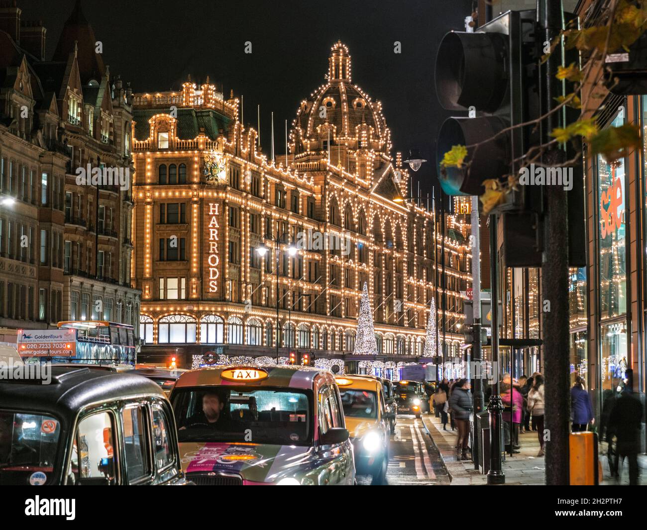 HARRODS TAXIS ULEZ LONDON NIGHT CHRISTMAS SHOPPING KNIGHTSBRIDGE Harrods Kaufhaus mit Lichtern in der Dämmerung mit Weihnachtslichtern Shopper und Taxen zum Mieten Knightsbridge London SW1 Stockfoto