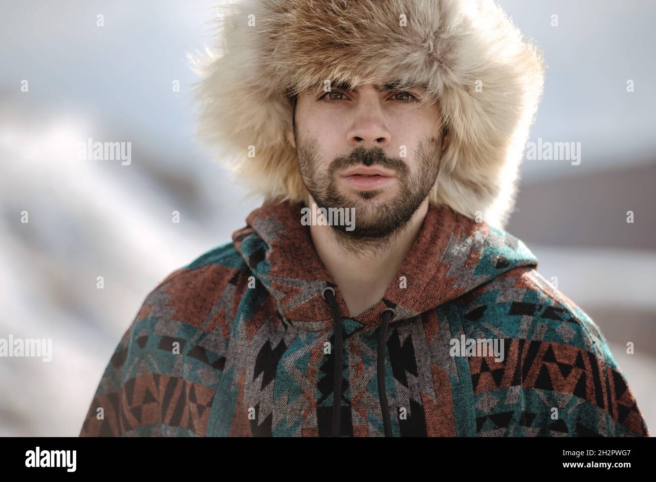 Porträt eines hübschen bärtigen Hipstermannes in arktischem Fuchshut und Poncho Stockfoto