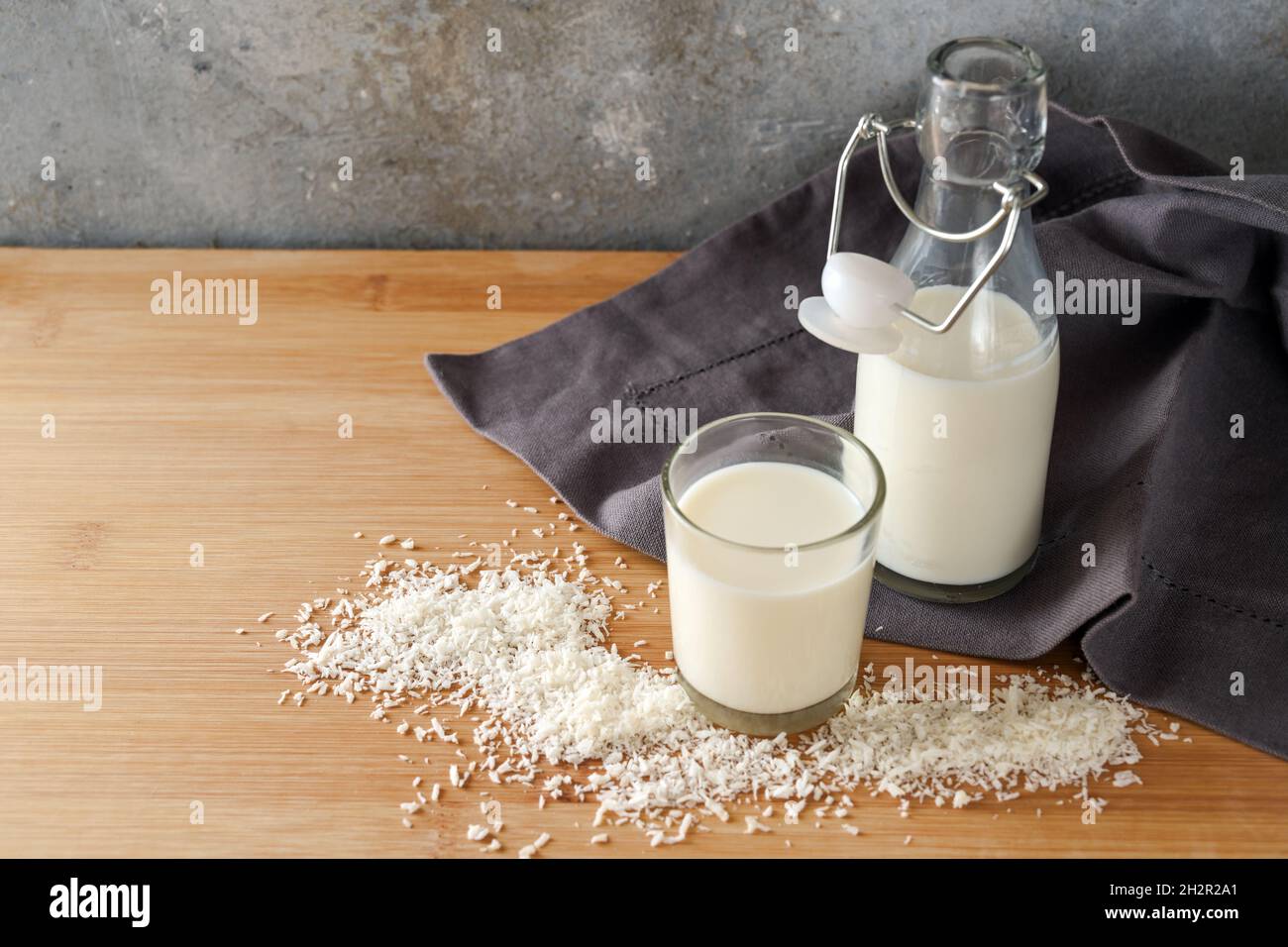 Vegane Kokosmilch und Flocken auf einer dunkelgrauen Serviette und einem Holztisch, tierfreundliche Alternative zu Milchprodukten, Kopierraum, ausgewählter Fokus, nar Stockfoto