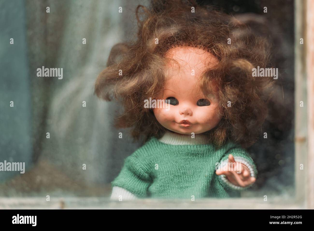 Nahaufnahme einer alten Puppe, die durch das Fenster guckt. Halloween-Konzept Stockfoto
