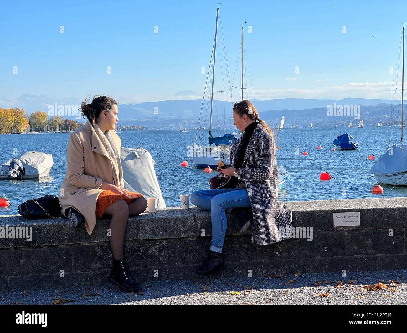 Zwei Freundinnen sitzen auf Betonbarriere am Zürichsee in der Schweiz