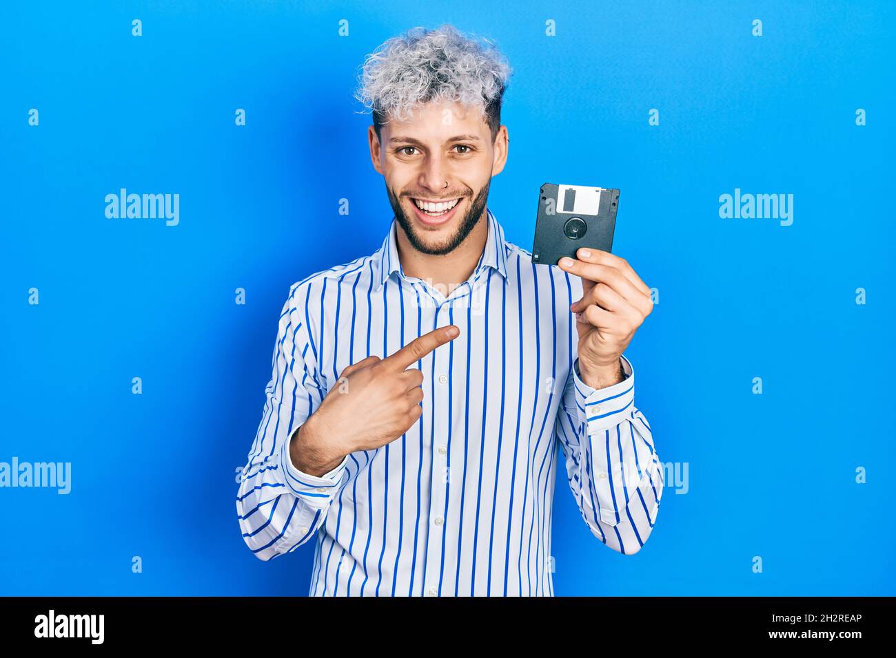 Junger hispanischer Mann mit modernen gefärbten Haaren, die Diskette mit lächelndem Lächeln und mit Hand und Finger zeigen Stockfoto